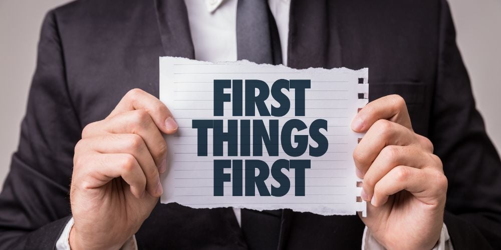 A person is holding a sign that says first things first, to demonstrate the first step of efficiency in the workplace.